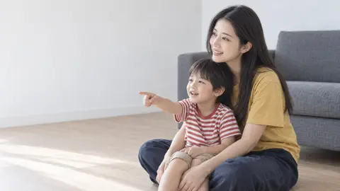 床に座り、テレビを指さして笑う子どもと女性