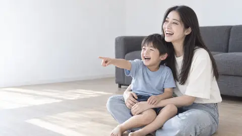 床に座り、テレビを指さして笑う子どもと女性