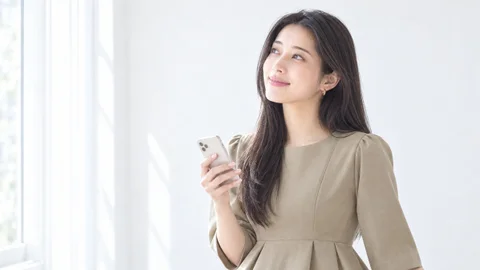 スマホを片手に持ち、斜め上を見て笑う女性